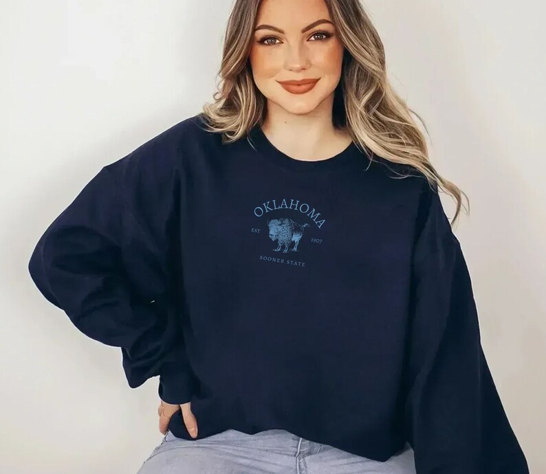 Puede incluir: Una sudadera azul marino con un gr&aacute;fico de un b&uacute;falo y el texto "Oklahoma Est. 1907 Sooner State".