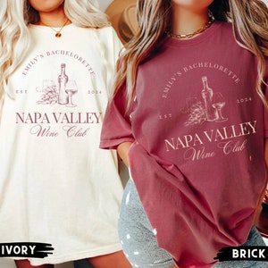 May include: Two women wearing t-shirts with the text "Emily's Bachelorette Est 2024 Napa Valley Wine Club". The shirt on the left is ivory and the shirt on the right is brick.