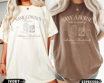 Puede incluir: Dos camisetas blancas con texto y gráficos marrones. La camiseta de la izquierda dice "Same Cowboy Forever" con un par de botas de vaquero y un vaso de whisky. La camiseta de la derecha dice "Save a Horse Ride a Cowboy" con un par de botas de vaquero y un vaso de whisky. Ambas camisetas dicen "Ashley's Bachelorette Nashville, TN" y "EST 2024". La camiseta de la izquierda es de color marfil y la camiseta de la derecha es de color espresso.