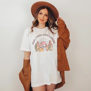 K&ouml;nnte beinhalten: Wei&szlig;es T-Shirt mit einem Aufdruck einer W&uuml;stenlandschaft und dem Text "Man, I feel like a bride".