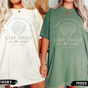 K&ouml;nnte beinhalten: Zwei &uuml;bergro&szlig;e T-Shirts mit einem Muschel-Motiv und dem Text "Emily's Bachelorette Est 2024 Last Toast on the Coast Miami Florida". Die Shirts sind in Elfenbein und Moosgr&uuml;n.