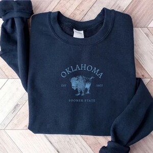 Puede incluir: Una sudadera azul marino con un gr&aacute;fico vintage de un b&uacute;falo y el texto "OKLAHOMA EST 1907 SOONER STATE".