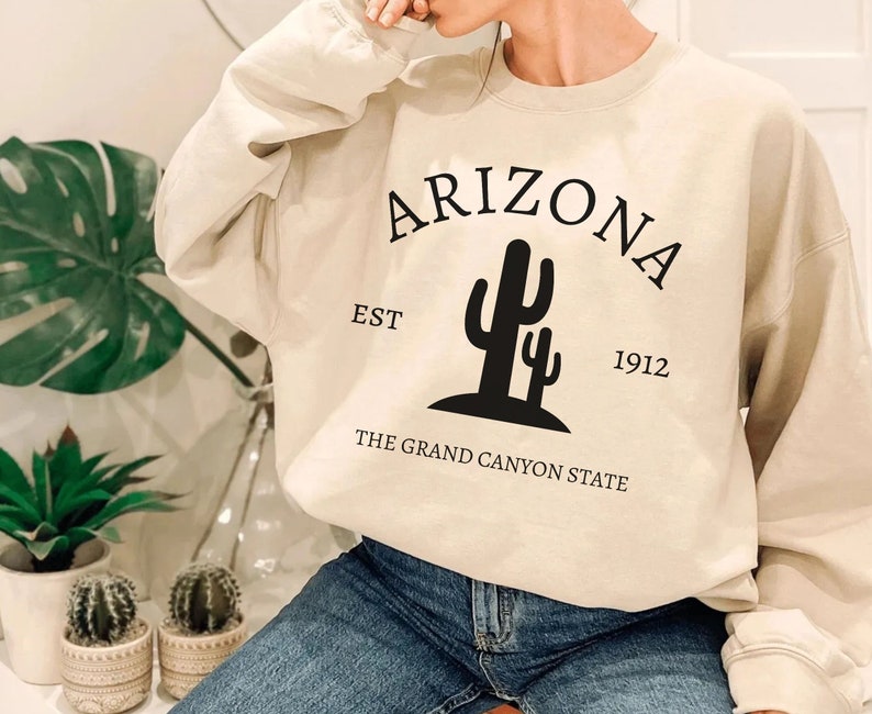 May include: A beige sweatshirt with the text "Arizona Est 1912 The Grand Canyon State" and a black silhouette of a cactus.
