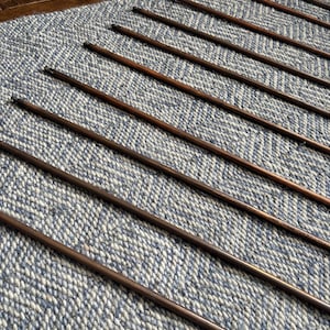 May include: Several thin, dark brown wooden dowels are laid diagonally across a blue and white textured rug. The dowels have a smooth, polished finish and are evenly spaced.