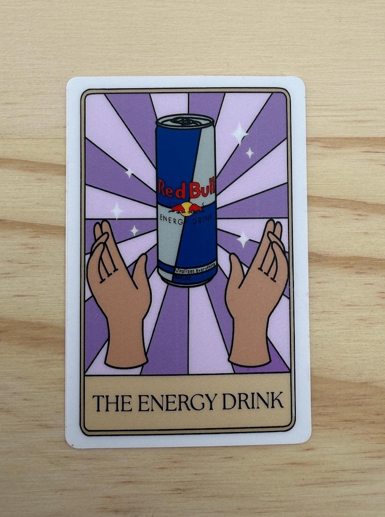 May include: A rectangular sticker featuring a Red Bull energy drink can in the center, set against a purple and white striped background. Two hands are positioned on either side of the can. The text "THE ENERGY DRINK" is at the bottom.