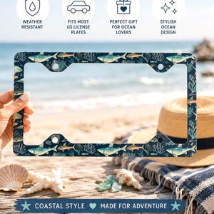 Puede incluir: Un marco de matrícula rectangular con un fondo azul oscuro y un patrón repetitivo de varios peces, tiburones y elementos de arrecifes de coral blancos. El marco cuenta con cuatro orificios de montaje circulares y una superficie plana.