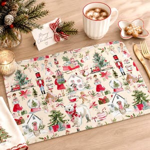 May include: A rectangular placemat featuring a festive watercolor print on a cream background. The pattern includes nutcrackers, Christmas trees, snow globes, gingerbread houses, gift boxes, and a polar bear wearing a red scarf.