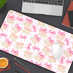 May include: A rectangular mouse pad with a white background featuring a repeating pattern of pink bows and stacks of books tied with pink ribbons. A computer mouse sits on the pad.