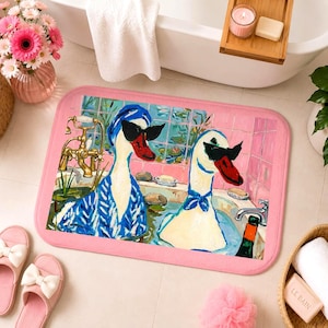 Peut inclure: Un tapis de bain rectangulaire à bordure rose illustrant deux canards blancs portant des lunettes de soleil noires et des accessoires de tête bleus, se relaxant dans une baignoire avec un robinet doré et des murs carrelés roses.