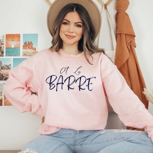 May include: A pink sweatshirt with the text "A La Barre" in navy blue lettering.