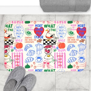 Puede incluir: Una alfombra de baño rectangular con un diseño caprichoso con patos, cruasanes, tazas de café y fresas. La alfombra tiene frases como "Los domingos están hechos para los cruasanes". Zapatillas grises en la parte inferior.