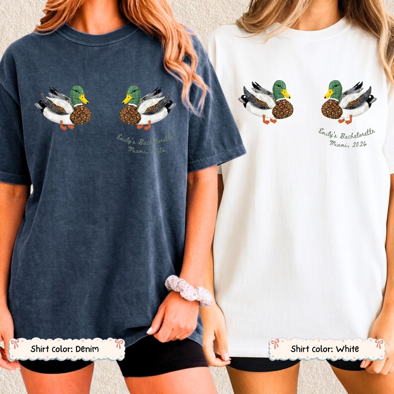 May include: Two short-sleeve crewneck t-shirts, one in denim blue and one in white, each featuring a graphic of two mallard ducks and the text "Emily's Bachelorette Miami 2026" printed in a script font below the right-hand duck illustration.