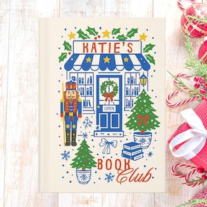 Könnte beinhalten: Ein cremefarbenes Notizbuch mit einer festlichen Illustration eines Buchladens mit dem Text "KATIE'S BOOK Club". Das Design umfasst einen Nussknacker, Weihnachtsbäume und Stechpalmen. Das Notizbuch ist mit Weihnachtsschmuck und Zuckerstangen verziert.