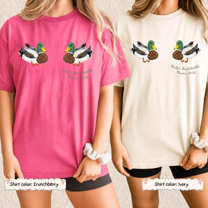 May include: Two short-sleeve t-shirts in crunchberry pink and ivory. Each shirt features a graphic of two mallard ducks with green plaid heads and brown patterned chests. Below the ducks, the text reads Emily's Bachelorette Miami 2026.