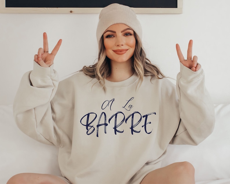 May include: A beige sweatshirt with the text "A La Barre" in navy blue script.