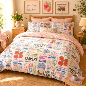 May include: A bedding set featuring a white duvet cover and pillowcases with a colourful print of farmers market produce, including tomatoes, strawberries, and asparagus, alongside text reading Farmers Market. The set includes a pink gingham border.
