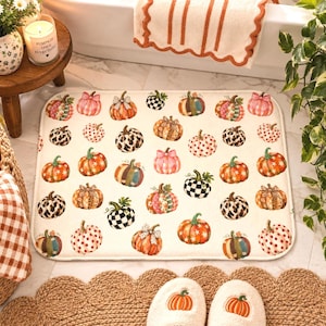May include: A rectangular bath mat with a cream-colored background featuring a repeating pattern of various pumpkins. The pumpkins display diverse designs including leopard print, black and white checkered patterns, polka dots, and floral motifs.