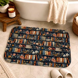 Puede incluir: Una alfombrilla de baño rectangular con un patrón repetitivo de estanterías azul oscuro llenas de libros multicolores, intercaladas con varias ilustraciones florales blancas, naranjas y rosas y hojas verdes dispuestas en varios estantes.