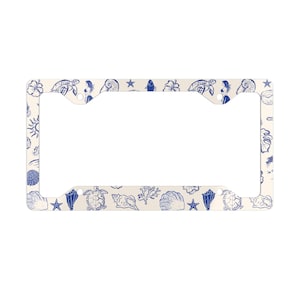 May include: License plate frame with a cream background and a repeating pattern of blue seashells, starfish, turtles, and hibiscus flowers. The frame has a rectangular shape with cutouts for the license plate.
