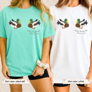 May include: Two short-sleeve t-shirts, one in island reef and one in white, each featuring a graphic of two mallard ducks and the text "Emily's Bachelorette Miami, 2026" printed on the chest. The ducks have green heads and brown patterned bodies.
