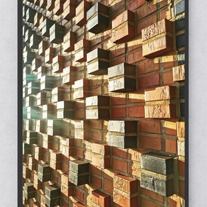 Könnte beinhalten: Eine Backsteinmauer mit einem Muster aus abwechselnd schwarzen und braunen Ziegeln. Die Ziegel sind in einem versetzten Muster angeordnet, wodurch ein dreidimensionaler Effekt entsteht. Die Wand wird von Sonnenlicht beleuchtet, das Schatten auf die Ziegel wirft.