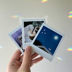 May include: Three instant photos with white borders. The first photo shows a plant in a pot with two iced coffees. The second photo shows a night sky with stars and a moon. The third photo shows a building with a power line.