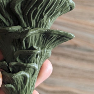 Op de afbeelding: Een 3D-geprinte groene paddenstoel met een textuur. De paddenstoel heeft een gelaagd ontwerp met meerdere lagen.