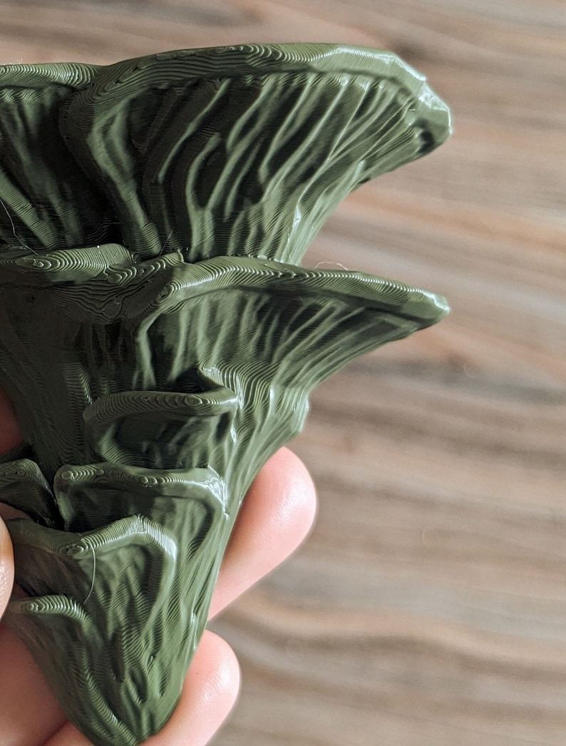 Op de afbeelding: Een 3D-geprinte groene paddenstoel met een textuur. De paddenstoel heeft een gelaagd ontwerp met meerdere lagen.