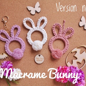 Pink macrame rabbits pendants with solid ears at cork board, next to flowers, Easter plywood eggs, butterflies. White Macrame Bunny Title. Version no 1 in the right top corner.
