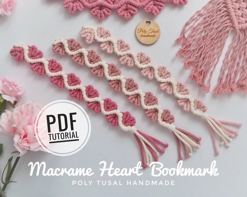 Op de afbeelding: Drie roze en witte macram&eacute; hartvormige bladwijzers met kwastjes. De bladwijzers zijn gemaakt met een roze kleurverloop. De afbeelding bevat de tekst "PDF TUTORIAL" en "Macrame Heart Bookmark POLY TUSAL HANDMADE".