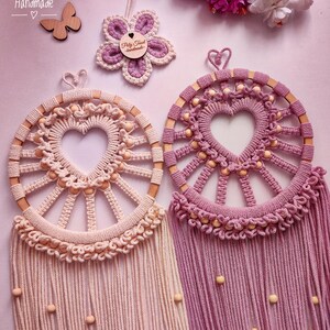 May include: Two handmade dreamcatchers with wooden hoops and heart-shaped centers. The dreamcatcher on the left is light pink with beige beads and the dreamcatcher on the right is a darker pink with beige beads.