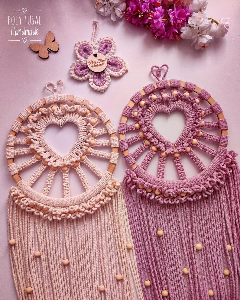 May include: Two handmade dreamcatchers with wooden hoops and heart-shaped centers. The dreamcatcher on the left is light pink with beige beads and the dreamcatcher on the right is a darker pink with beige beads.