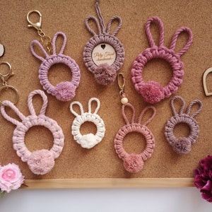 Pink macrame rabbits pendants with solid and thin ears at cork board, next to flowers, Easter plywood hearts, butterflies.