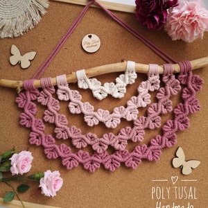 Pink version of Macrame Leaf Half Mandala laying on the cork board with pink flowers.  Next to Mandala are wooden butterflies.
On the right edge is logo of Poly Tusal Handmade.