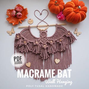 May include: A dusty rose macrame bat wall hanging with fringe and wooden flower accents. The text "MACRAME BAT Wall Hanging" is displayed. Decorative pumpkins, leaves, and wooden butterflies are also present.