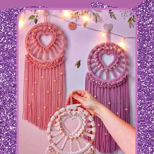May include: Two macrame heart dream catchers, one pink and one purple, with wooden beads and fringe. The dream catchers are hanging on a wall with string lights. The text "MACRAME HEART DREAM CATCHER PDF TUTORIAL" is at the top of the image. The text "Copyright 2025 Designed by Poly Tusal Handmade" is at the bottom of the image.