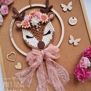 Cute sleeiing macrame deer with flower wreath on the forehead. The head is attaching to the plywood hoop. Over the neck is attaching a pink lace ribbon. Pink flowers in the edges of the photo.