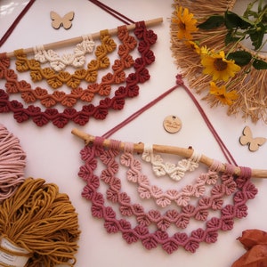 Macrame Leaf Half Mandalas laying on the white board with yellow flowers, cotton cords.  Mandalas are in 2 different colors, on the left warm colors (ecru, mustard, terracotta, red) and on the right the shades of pink version.