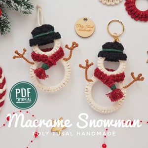 Peut inclure: Une décoration de Noël en macramé en forme de bonhomme de neige blanc avec une écharpe rouge et dorée, un chapeau noir et un pompon doré. L'ornement est suspendu à une ficelle blanche. L'image comprend également un tutoriel PDF pour la réalisation de l'ornement.