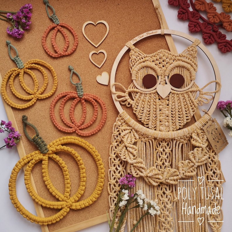 May include: A macrame owl wall hanging with a wooden hoop and fringe. The owl is made with natural coloured yarn and has brown eyes. There are also three macrame pumpkin ornaments in orange and yellow.