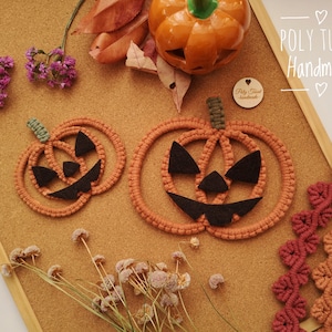 May include: Two orange crocheted pumpkin decorations with black felt faces. The pumpkins are on a cork board with autumn leaves and a small wooden sign that says "POLY TUSAL Handmade".