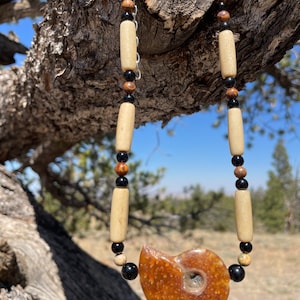 May include: A necklace made with brown, black, and white beads, with a large, orange, fossilized ammonite pendant.