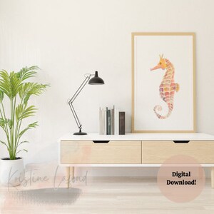 Puede incluir: Una impresi&oacute;n en acuarela enmarcada de un caballito de mar en tonos naranja, rosa y morado. El caballito de mar es el punto focal, sobre un fondo blanco dentro de un marco de madera clara. La impresi&oacute;n se exhibe en un mueble blanco y de madera.