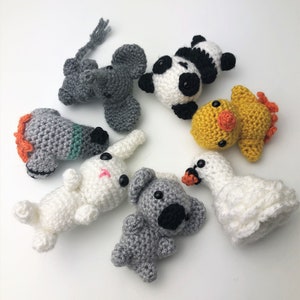 May include: A collection of seven crocheted stuffed animals, including a panda, a swan, a duck, a koala, a rabbit, and an elephant. The animals are all different colours and have different facial expressions.