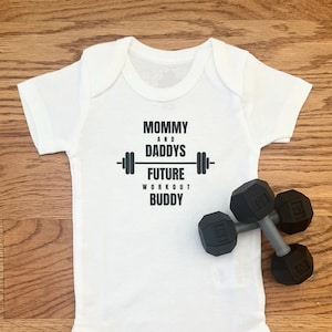 Set of "Mommy and Daddys Future Workout Buddy" Infant Bodysuit and 2 Dumbbell Rattles. Great gift for exercise enthusiasts and new parents!