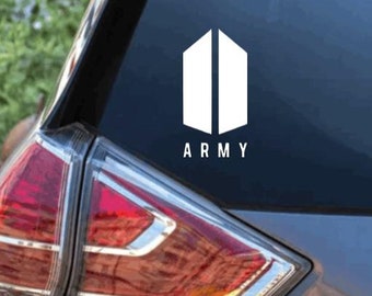 Puede incluir: Una calcomanía de vinilo blanco aplicada en la ventana trasera de un coche gris. La calcomanía presenta un logotipo geométrico que consiste en dos trapecios verticales uno al lado del otro, con la palabra ARMY impresa debajo del icono.