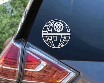 May include: A white vinyl decal featuring the spherical Death Star space station design with its signature concave dish and geometric paneling, applied to the rear window of a dark-colored hatchback vehicle, centered on the glass surface.