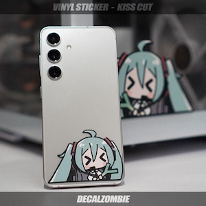 May include: A silver smartphone with a vinyl sticker of a cartoon character with teal hair and headphones. The sticker is on the back of the phone. The text "VINYL STICKER - KISS CUT" is at the top, and "DECALZOMBIE" is at the bottom.