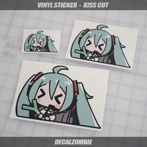 May include: Three vinyl stickers with a cartoon character design. The character has teal hair, a black outline, and is on a white background. The stickers are labeled "VINYL STICKER - KISS CUT" and "DECALZOMBIE".