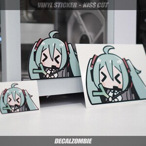 May include: Vinyl sticker featuring a cartoon character with teal hair and red accents. The sticker has a kiss-cut design and is available in multiple sizes. The text "VINYL STICKER - KISS CUT" and "DECALZOMBIE" are visible.
